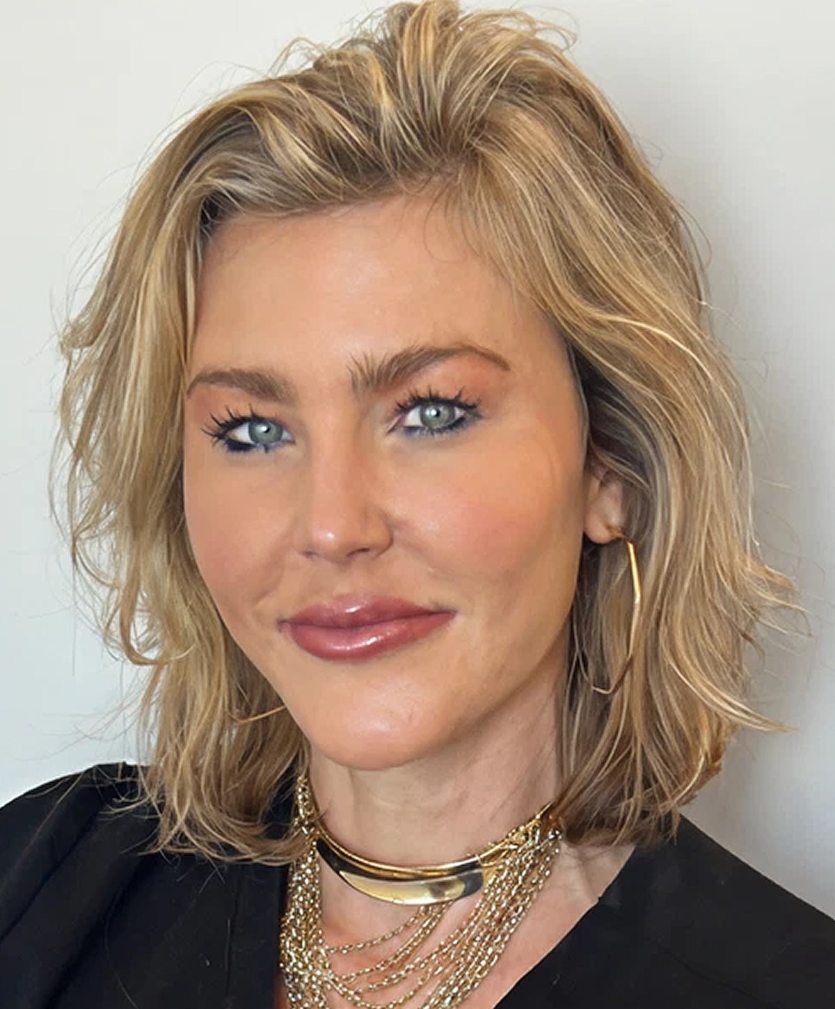 Smiling woman with layered blonde hair and jewelry.