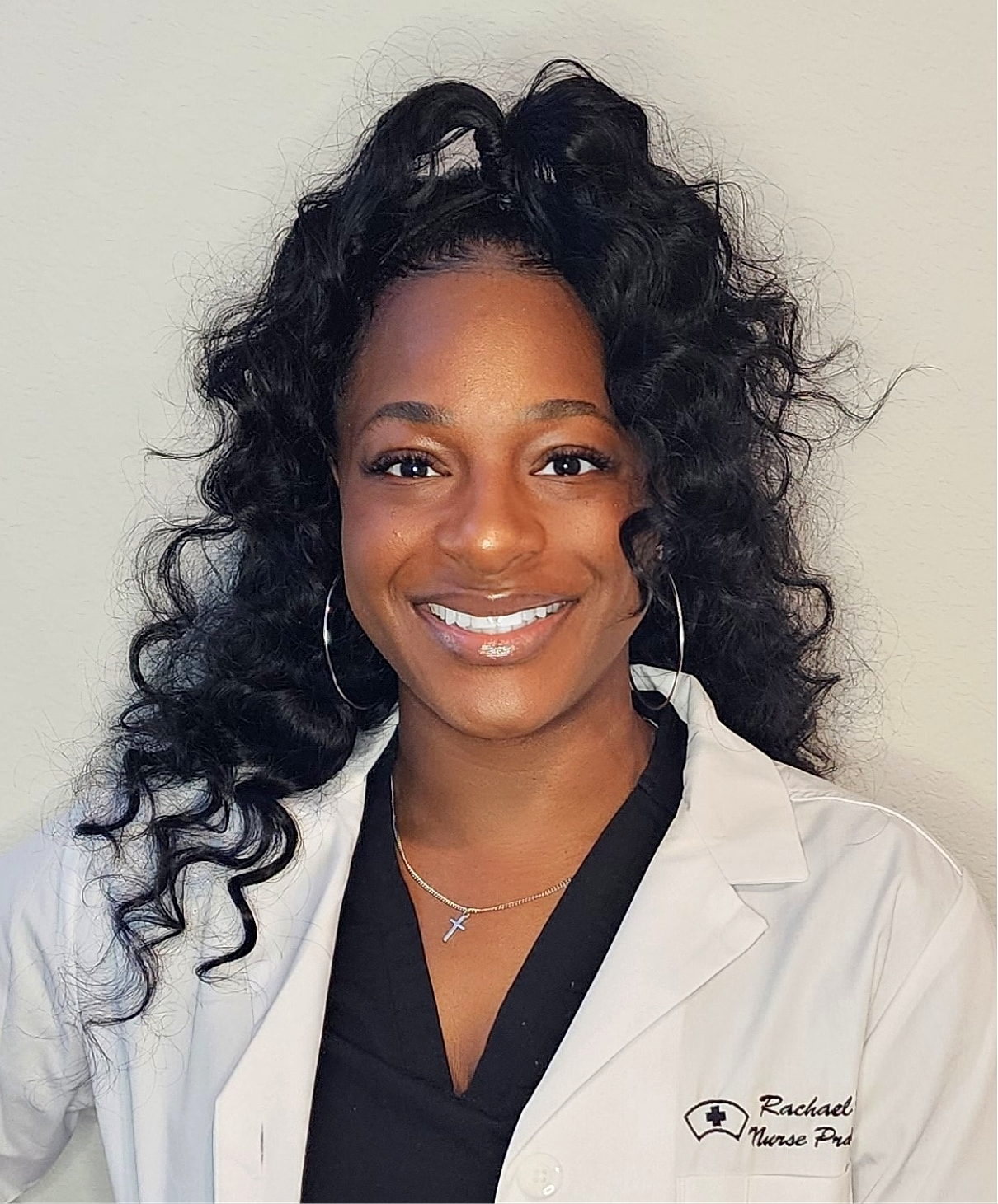 Smiling nurse in professional attire with curly hair.