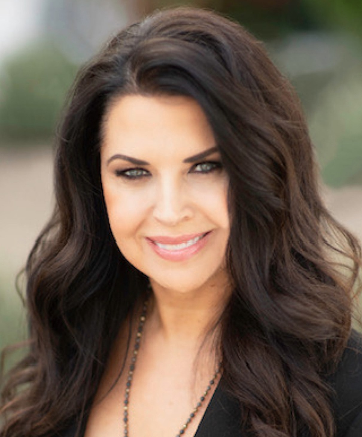 Smiling woman with long, wavy hair outdoors.