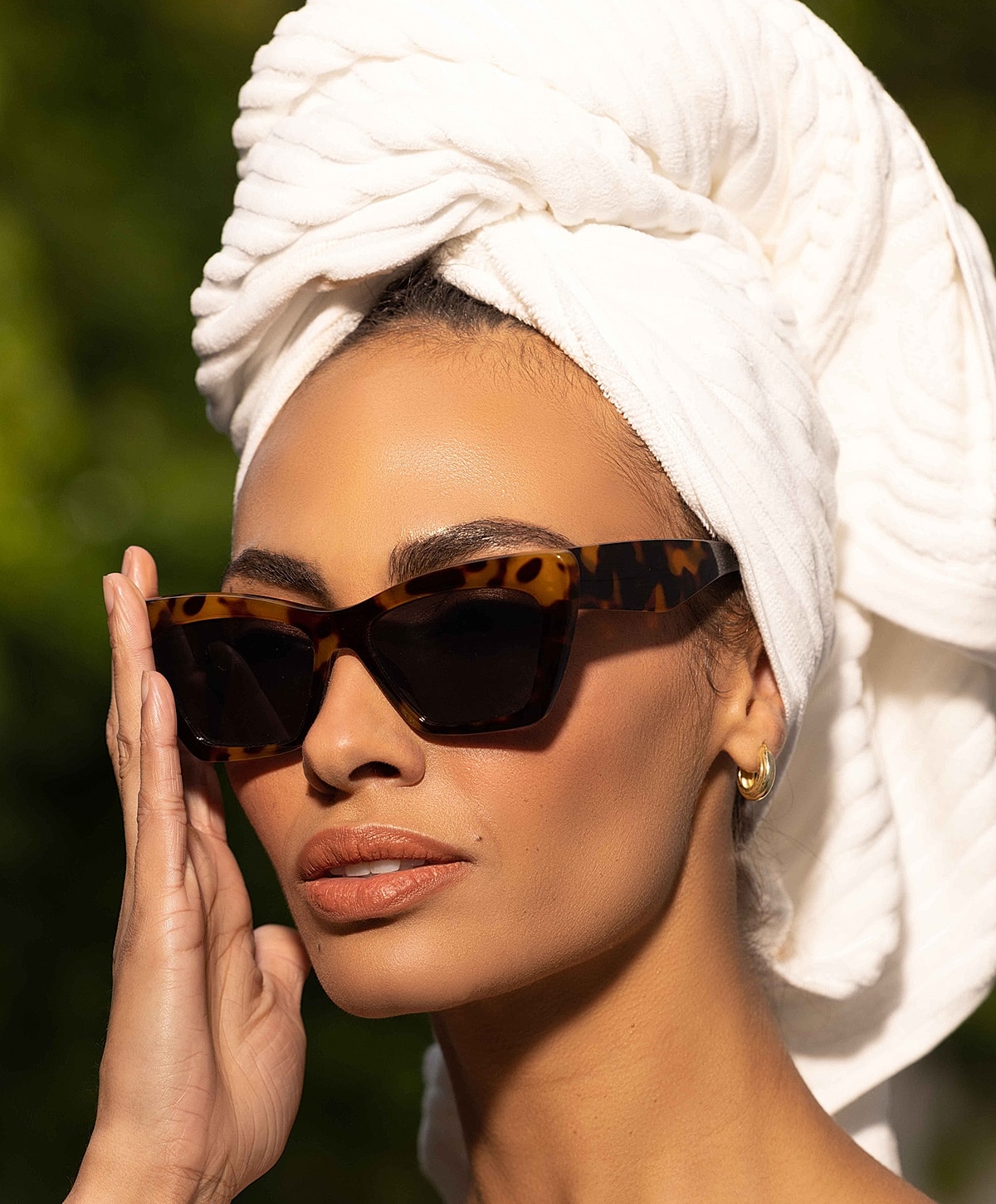 Woman in sunglasses with towel on head.