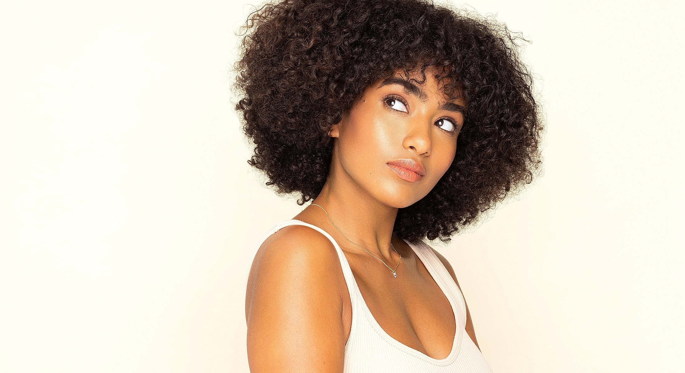 Woman with curly hair looking thoughtfully to side.