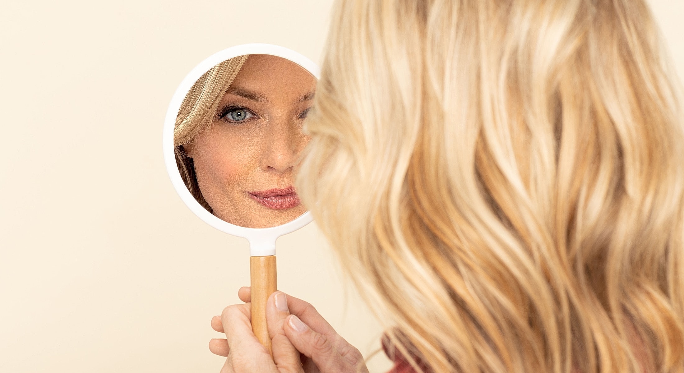 Woman looking at herself in a hand mirror.